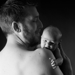 Niestadt-Fotografie-Schoonhoven-Newborn-shoot-vader-met-dochter-over-zijn-schouder-sfeervol-tegen-een-donkere-achtergrond